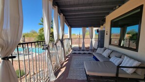A covered outdoor seating area with a pool in the background.