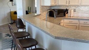 A modern kitchen with a bar area, white cabinets, and a tiled backsplash.