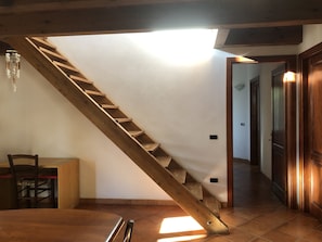 Un escalier en bois menant à un deuxième étage, un coin repas avec une table et des chaises, et un couloir avec des portes en bois.
