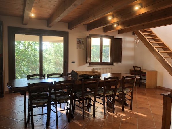 Un coin repas avec une table et des chaises en bois, une fenêtre donnant sur les arbres et un escalier en bois.