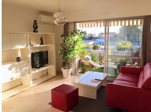 A living room with a TV, red sofa, and a balcony with plants.
