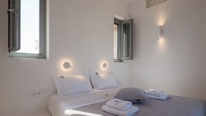 A bedroom with a bed, pillows, a bedside table, and a window. - Bracket House Paros Villa with Private Pool Sleeps 8 (Paros)