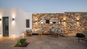 A modern outdoor seating area with stone walls and a white building. - Bracket House Paros Villa with Private Pool Sleeps 8 (Paros)
