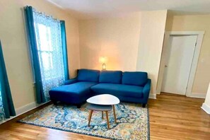 Una sala de estar con un sofá azul, una mesita redonda y un tapete estampado.