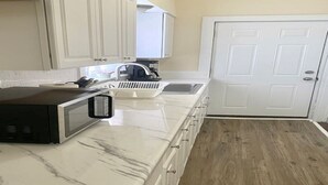 Una cocina con armarios blancos, un microondas, un fregadero y una puerta.