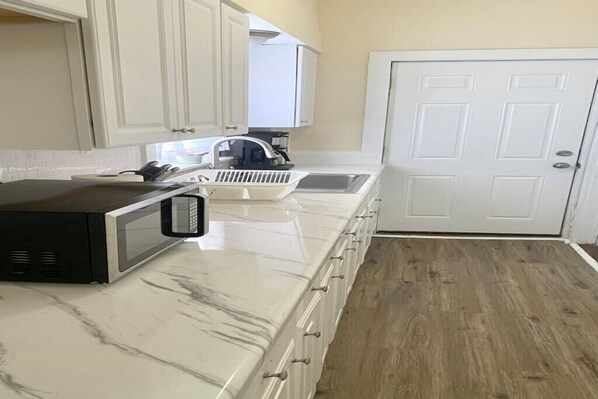 Una cocina con armarios blancos, un microondas, un fregadero y una puerta.