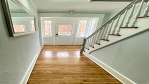 Un pasillo con suelo de madera, paredes blancas y una escalera con balaustres blancos.