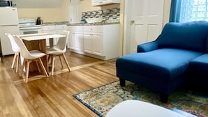 Una sala de estar moderna con un sofá azul, una mesa blanca y una zona de comedor con sillas blancas y una mesa de madera.