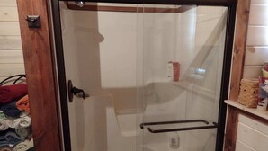 A glass-enclosed shower area with a wooden frame, a towel rack, and a toilet visible through the glass. - Riverfront Property Great for Fishing or Just Relaxing (Hesperia)