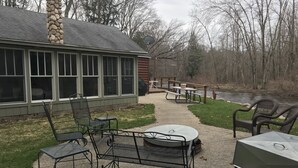 An outdoor patio with metal chairs and tables, a stone chimney, and a view of a river. - Riverfront Property Great for Fishing or Just Relaxing (Hesperia)