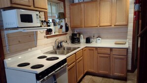A compact kitchen with a stove, microwave, sink, and wooden cabinets. - Riverfront Property Great for Fishing or Just Relaxing (Hesperia)