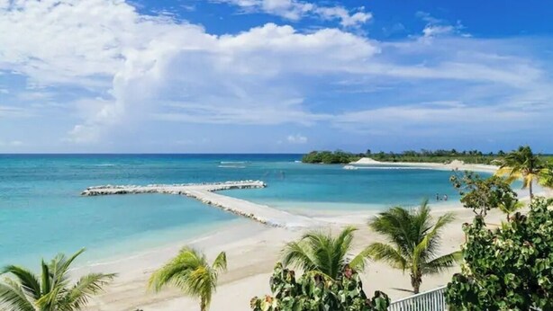 Een strand met helder turquoise water, wit zand en palmbomen.