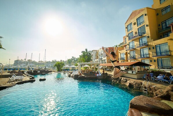 A swimming pool with lounge chairs and a building with balconies.
