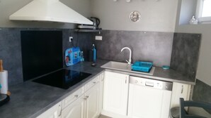 A compact kitchen with white cabinets, a black stove, a white range hood, a sink with a blue soap dish, and a wall-mounted clock.