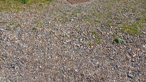 A gravel driveway leading to a white building with a door and a hanging macrame chair.