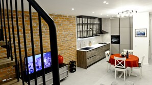 Une cuisine moderne avec un mur en briques, un îlot central en bois et un coin repas agrémenté d’une nappe rouge.