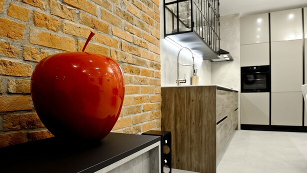 Une cuisine moderne avec un mur en briques, une grande sculpture représentant une pomme rouge et un élégant plan de travail noir.