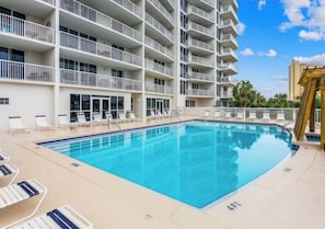 A swimming pool with lounge chairs and a multi-story building with balconies.