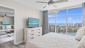Ein Schlafzimmer mit einem großen Bett, einem Deckenventilator, einem Fernseher und Blick auf Stadt und Wasser.