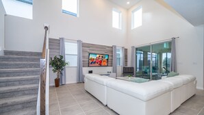 A modern living room with a staircase, a large flat-screen TV, a white sofa, and a dining area with a glass door. - (EE2098) SANITIZED 5/4.5 Private Pool & Jaccuzi & Free Waterpark (Kissimmee)