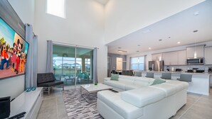 A modern living room with a white sofa, a coffee table, and a TV. There is a kitchen area with a microwave and a refrigerator. - (EE2098) SANITIZED 5/4.5 Private Pool & Jaccuzi & Free Waterpark (Kissimmee)