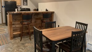 Una cocina compacta con armarios de madera, un refrigerador negro y una mesa de madera con cuatro sillas.