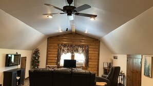 Una sala de estar acogedora con ventilador de techo, chimenea, televisor y un árbol de Navidad.