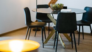 Een moderne eetruimte met een ronde tafel, zwarte stoelen, een hanglamp en een houten balkenstructuur.