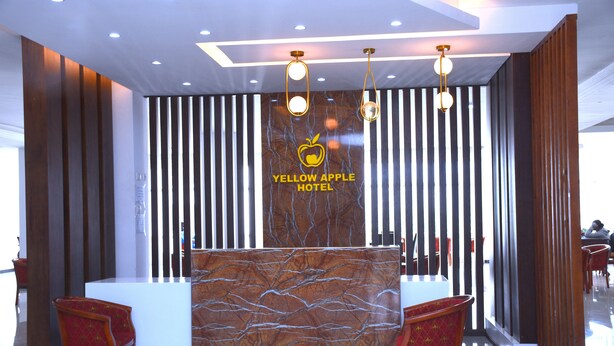 A reception desk with a marble-like design, a logo reading "Yellow Apple Hotel," and two red upholstered chairs. - yellow apple hotel (Addis Ababa)