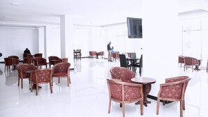 A spacious, well-lit room with multiple seating areas, including red upholstered chairs and a few wooden tables. - yellow apple hotel (Addis Ababa)