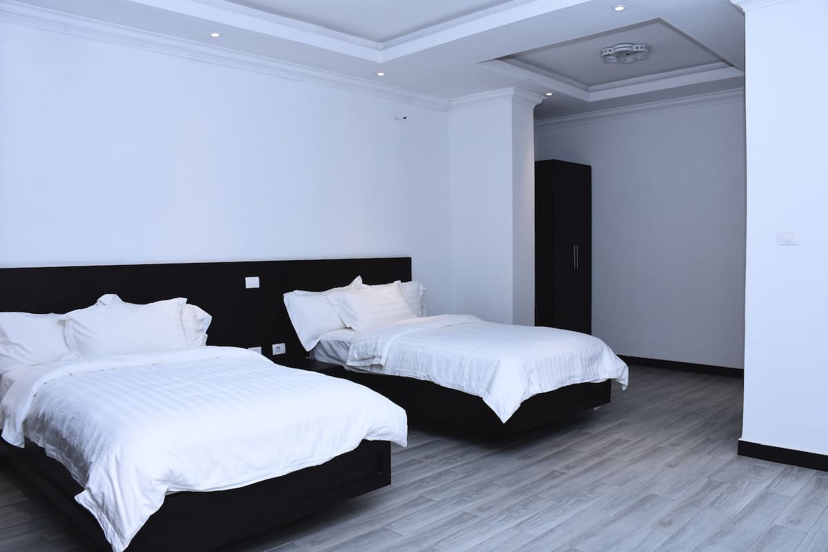 A modern hotel room with two beds, a dark headboard, and a light wooden floor.