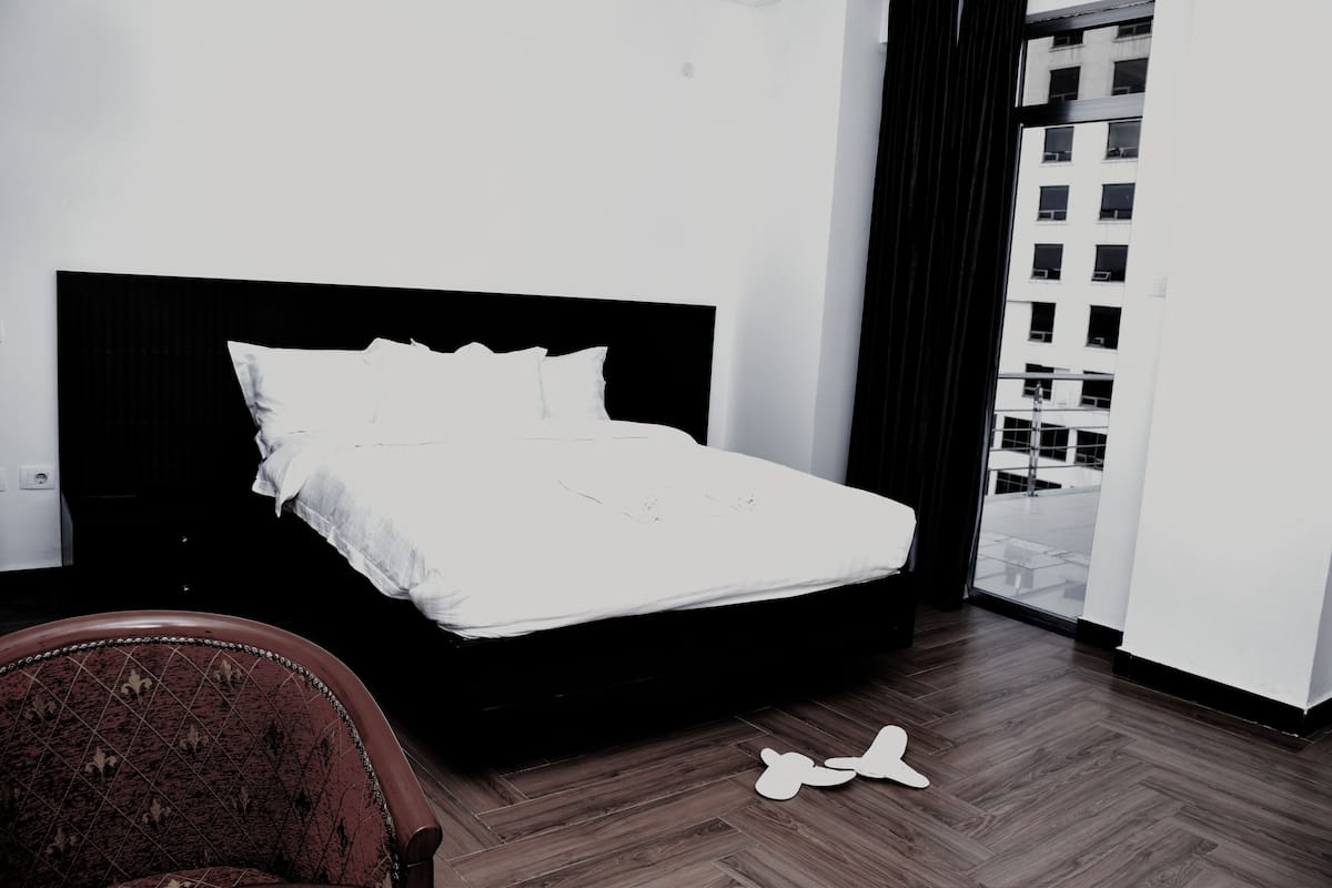A hotel room with a bed, a chair, and a view of a building through a window.