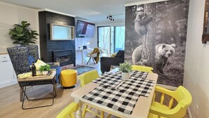 A dining area with a checkered tablecloth, yellow chairs, and a large bear-themed wall art.