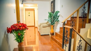 A hallway with a wooden staircase, a beige sofa, a potted plant, and a vase with red flowers. - Sol de los Andes Machupicchu (Machu Picchu)