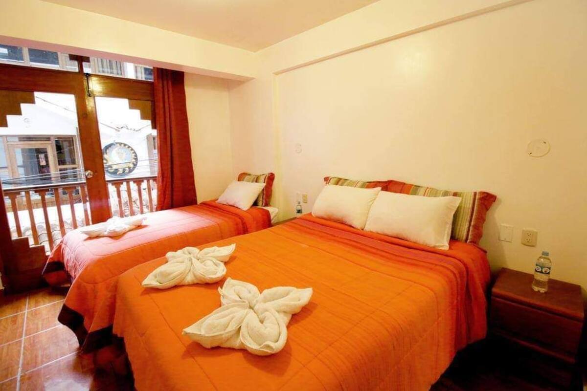 A hotel room with two beds, each with an orange bedspread and white pillows. There is a wooden nightstand with a water bottle on it.