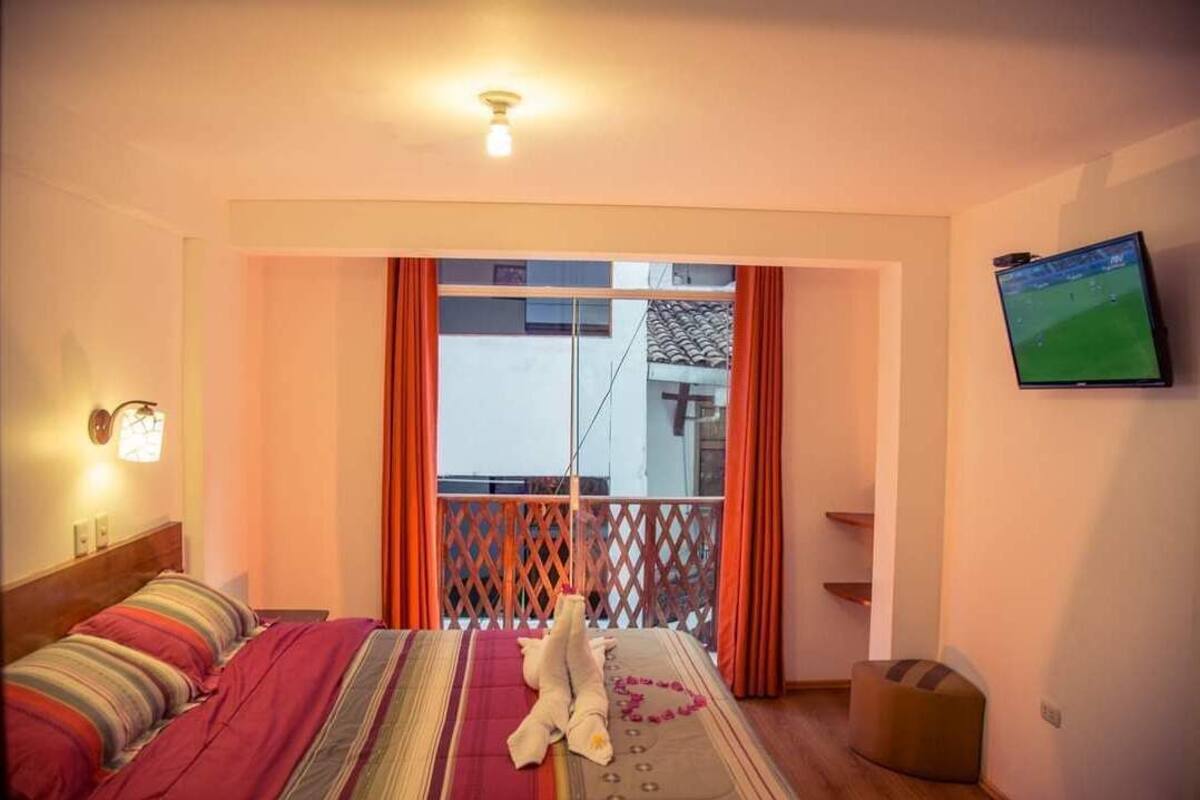 A hotel room with a bed, a TV on the wall, and a balcony with a view.