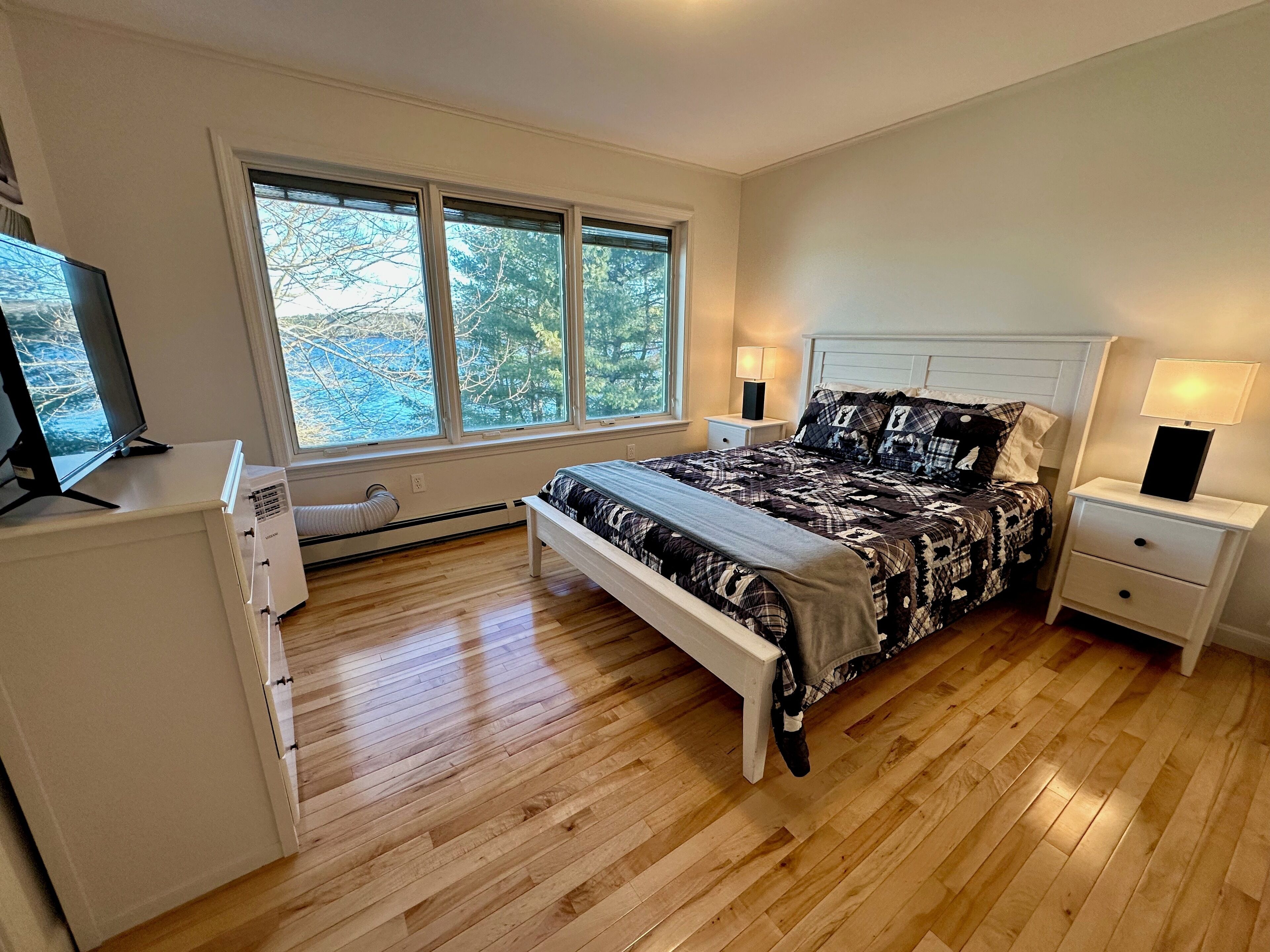 A bedroom with a bed, bedside tables, a desk, and a window with a view of trees.