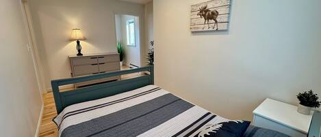 Et soveværelse med seng, natbord, lampe, kommode og et billede på væggen.