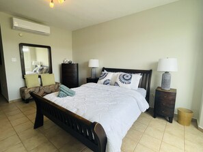 Un dormitorio con cama, dos mesitas de noche, cómoda, espejo y aire acondicionado instalado en la pared.