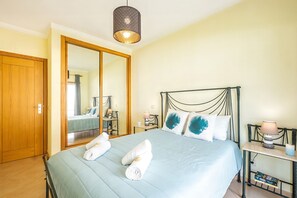 Een slaapkamer met een bed, nachtkastje met lamp, spiegel en kledingkast.