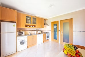 Une cuisine moderne avec des meubles en bois, un lave-linge, un four à micro-ondes et un panier à fruits.