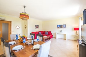 A dining area with a wooden table set for four, a red sofa, a small white table, and a TV stand with a flat-screen TV. - Elegant Apartment near the Beach (Alvor)
