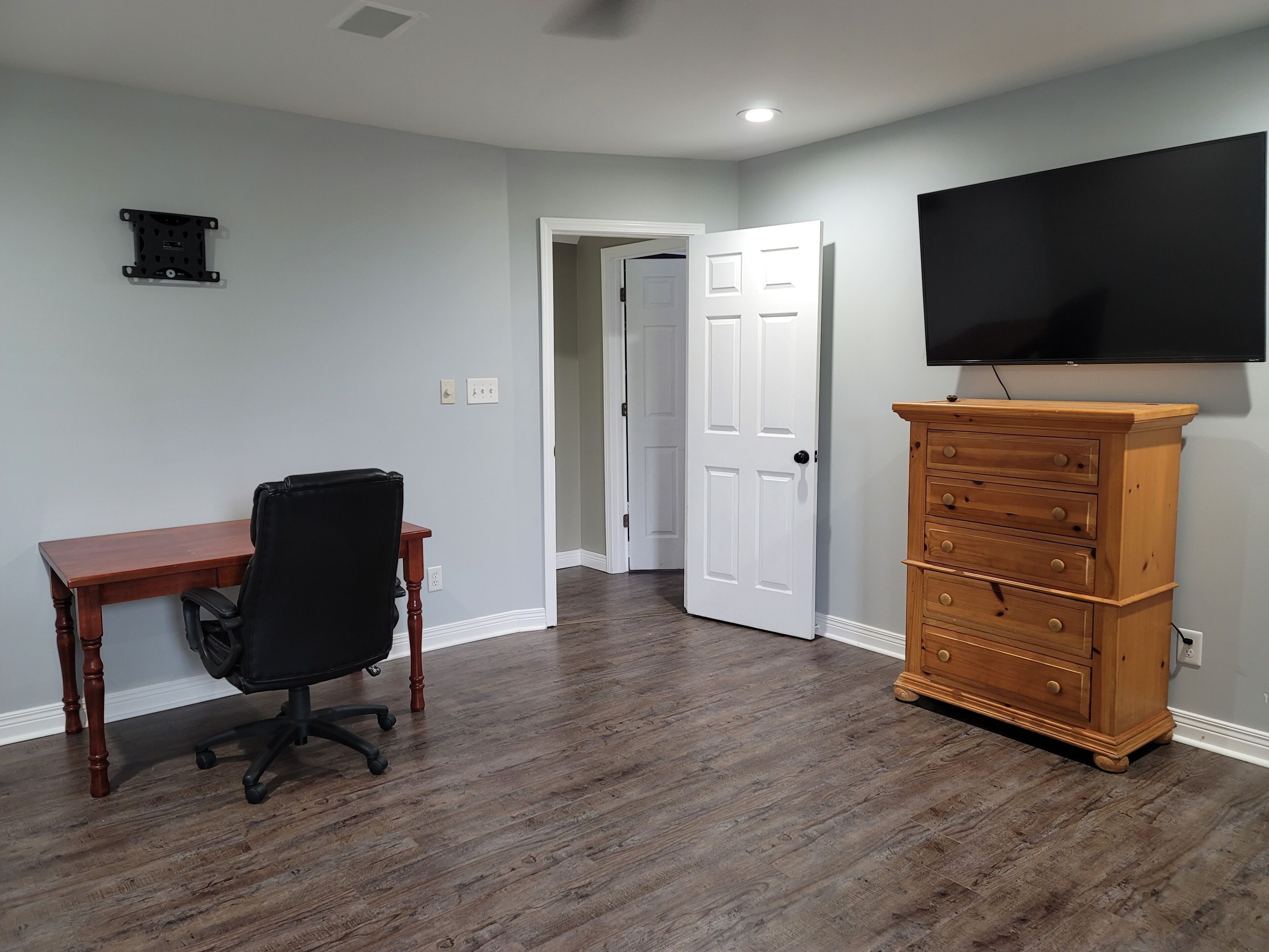A room with a wooden desk, black office chair, and a wooden dresser with drawers.