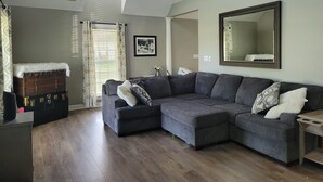 A modern living room with a sectional sofa, a large mirror, and a window with curtains.