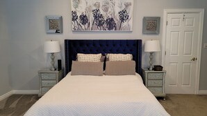 A bedroom with a large bed, two nightstands, a door, and wall art.
