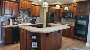 A modern kitchen with wooden cabinets, granite countertops, stainless steel appliances, and pendant lighting.