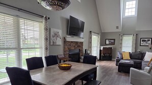 A spacious living room with a fireplace, a dining table, and a large window.