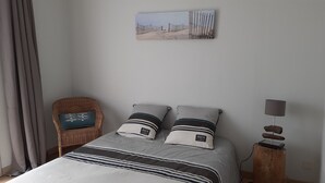 Ein Schlafzimmer mit einem Bett, zwei Kissen, einem Sessel, einer Lampe und einem Gemälde an der Wand.