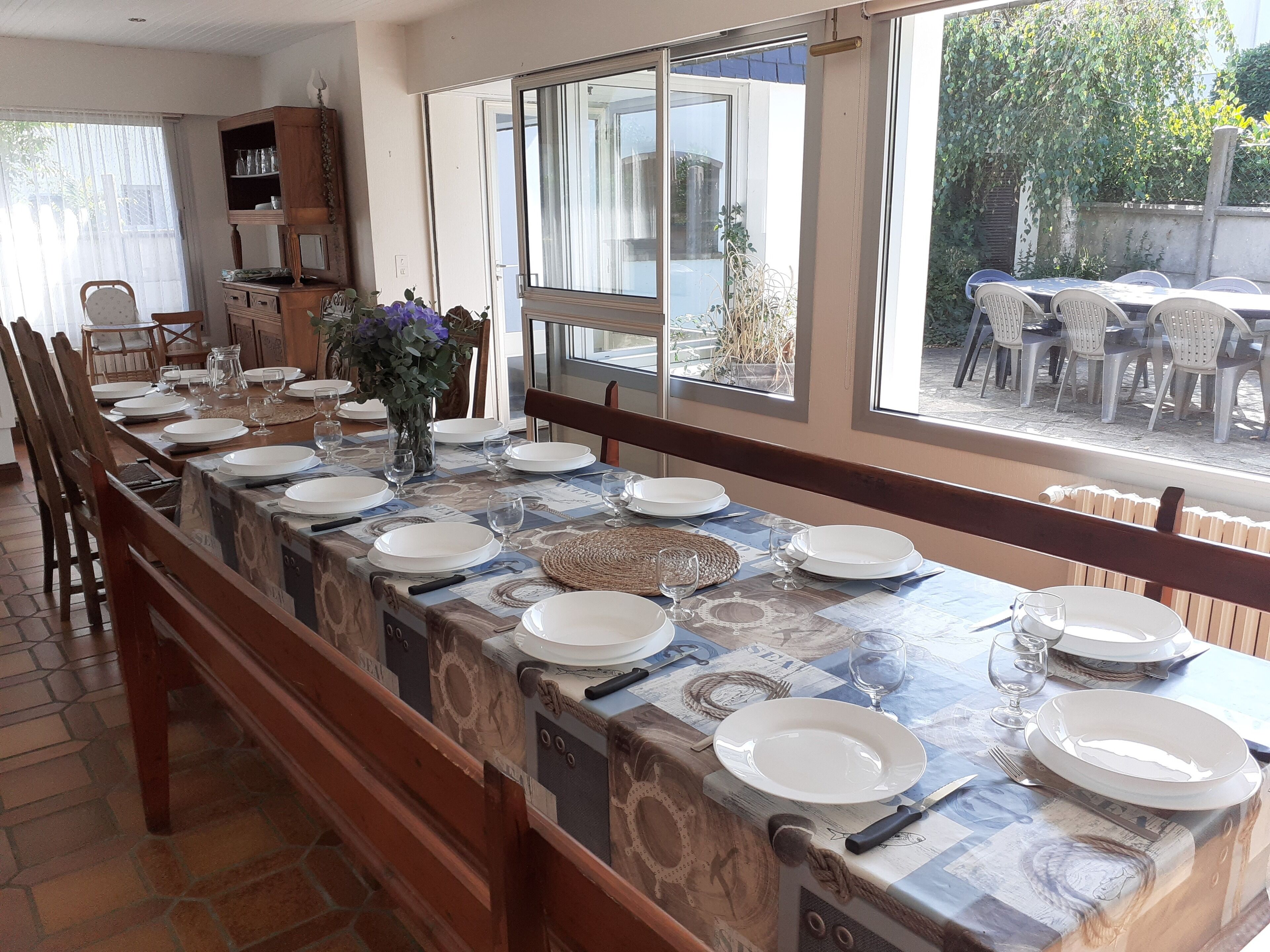 A long dining table set with plates, glasses, and cutlery, flanked by chairs.