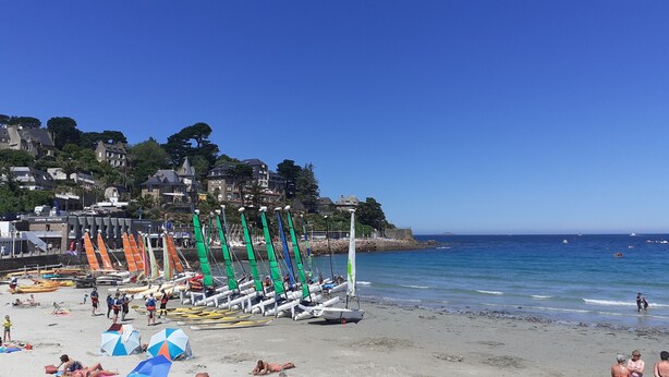 Ein Strand mit Segelbooten, einer Sandküste und Gebäuden im Hintergrund.